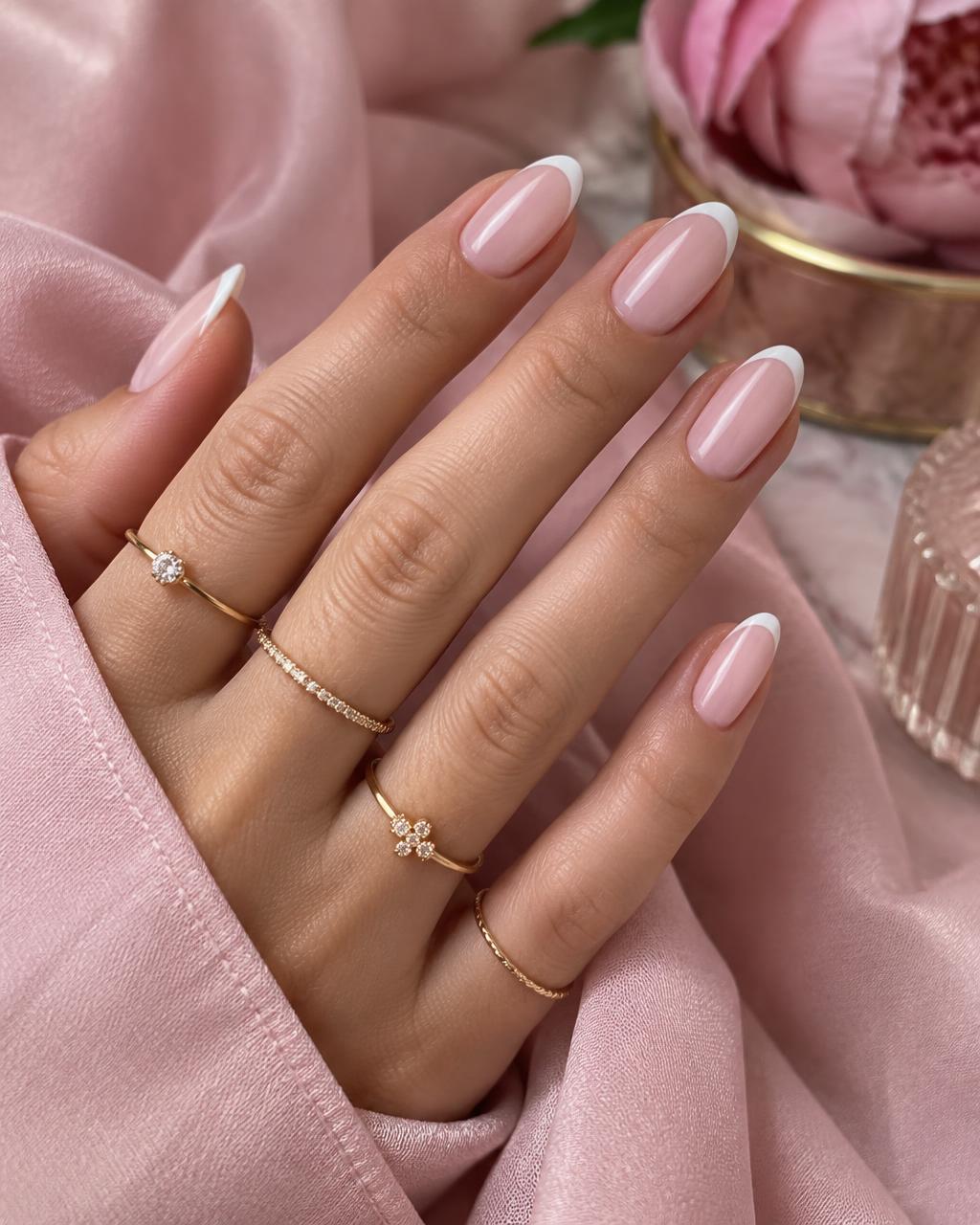 Mão com unhas em francesinha delicada e anéis dourados sobre tecido rosé